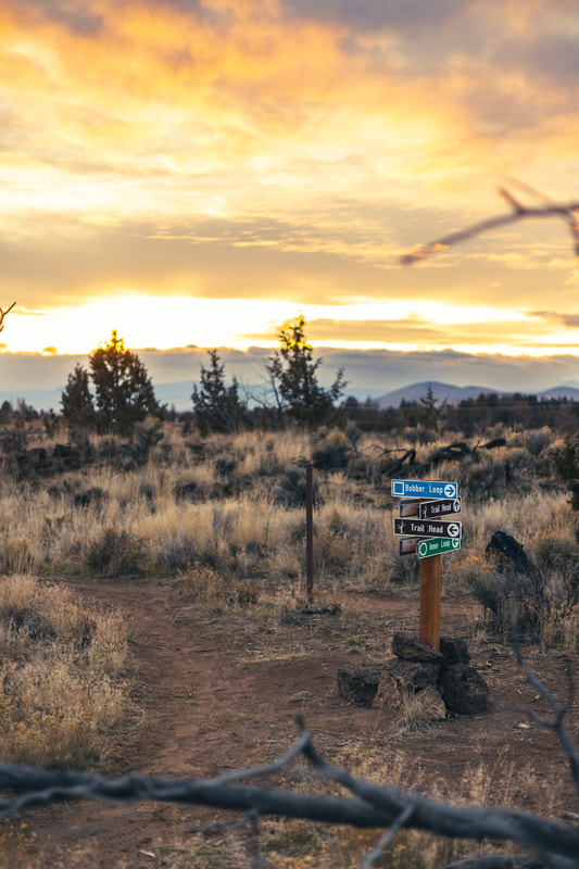 Wooden post with signs for Bobber Loop, Inner Loop, and trailhead signs against mountains and the setting sun in the background